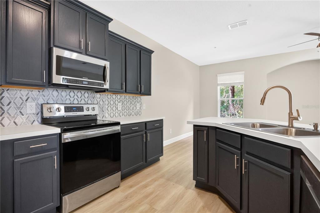 A kitchen features dark cabinets, stainless steel appliances, a patterned backsplash, and a corner sink — 15357 OAK APPLE COURT UNIT 4C, WINTER GARDEN, FL