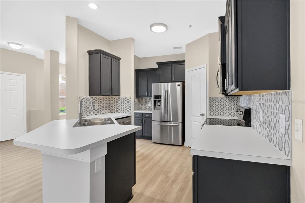 A kitchen features dark cabinets, white countertops, a patterned backsplash, and light wood-look flooring — 15357 OAK APPLE COURT UNIT 4C, WINTER GARDEN, FL