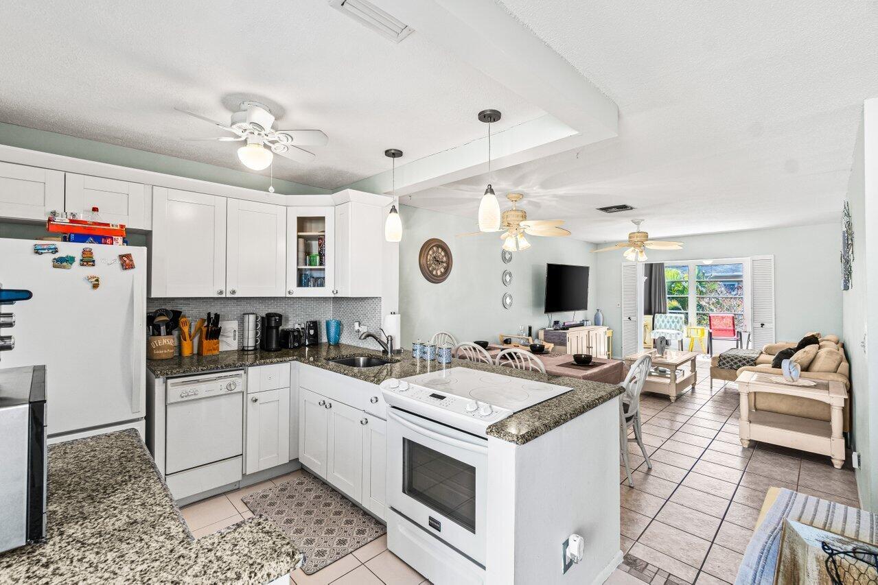 A kitchen with white cabinets and granite countertops opens into a living area with tile — 2121 NE 1st Court # 202, Boynton Beach FL 33435, BOYNTON BEACH, FL