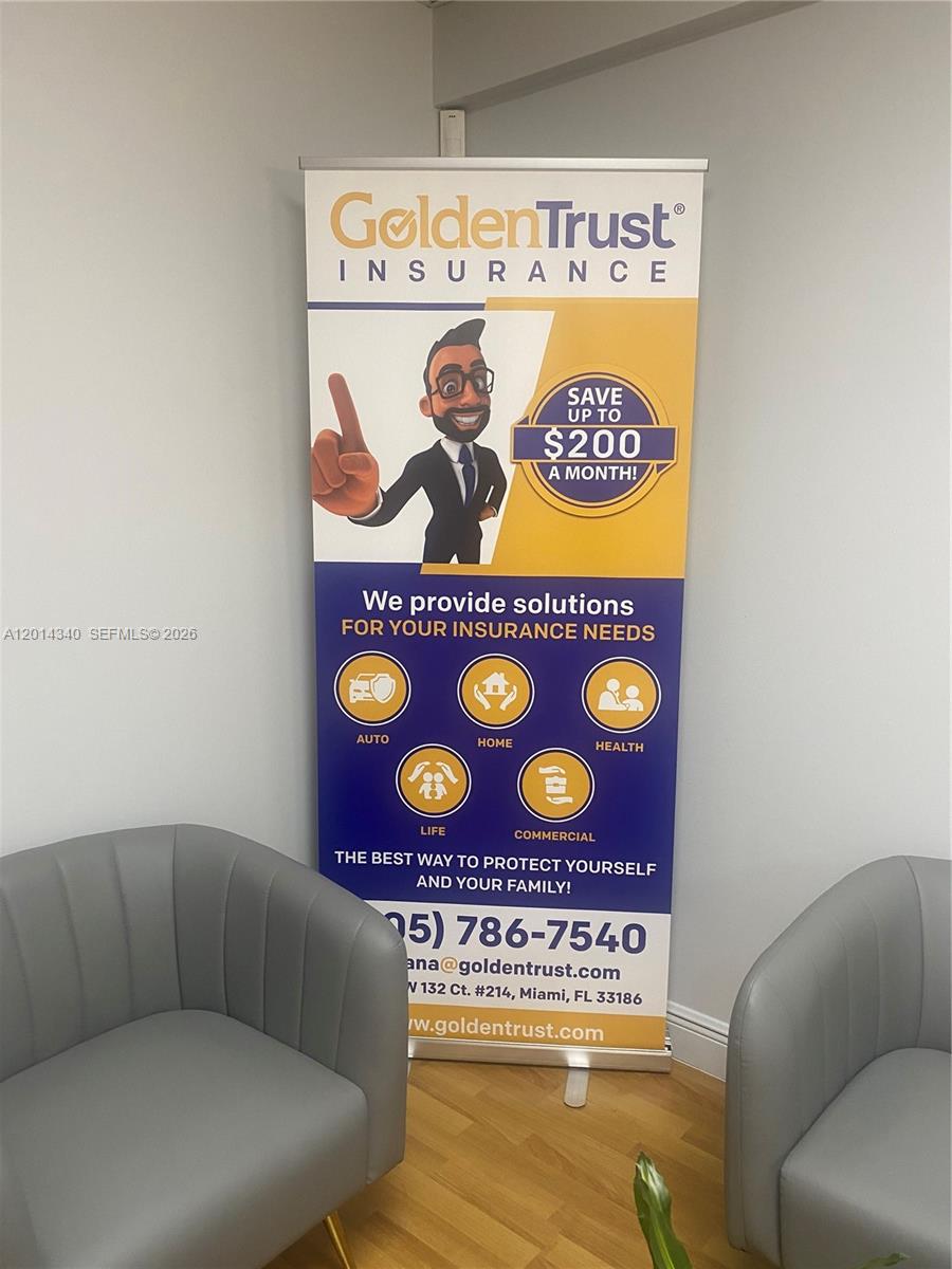 A vertical banner for GoldenTrust Insurance stands between two gray armchairs in a room — 12350 SW 132nd Ct, Miami FL 33186, MIAMI, FL