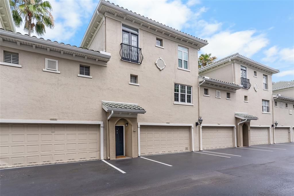 The exterior of a multi-story townhouse complex features beige stucco walls and attached garages — 501 KNIGHTS RUN AVENUE UNIT 5102, TAMPA, FL