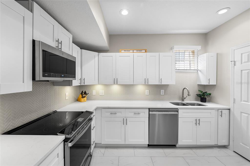 A modern kitchen features white cabinets, stainless steel appliances, a herringbone backsplash, and white countertops — 501 KNIGHTS RUN AVENUE UNIT 5102, TAMPA, FL