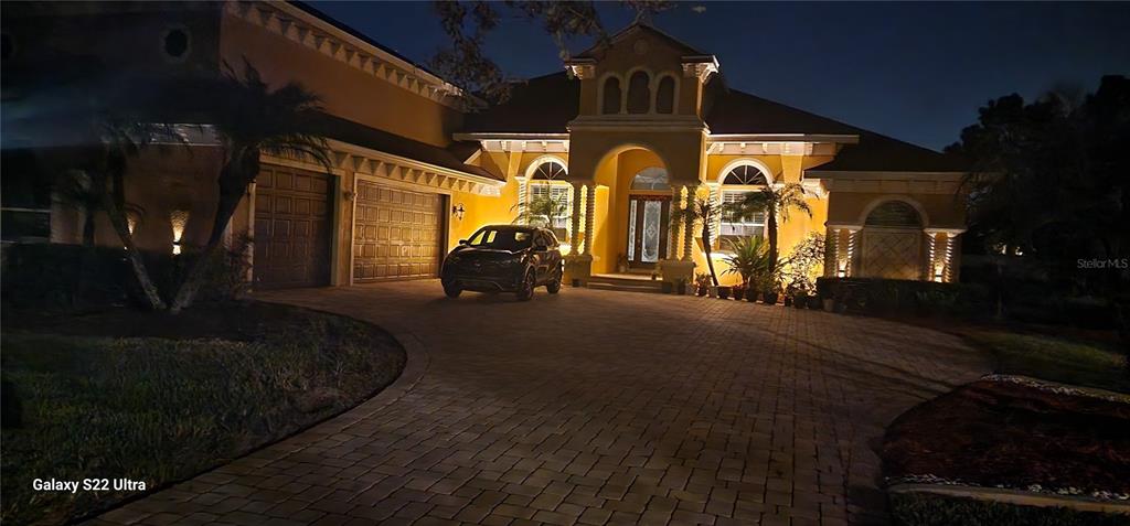 A night view of a yellow house with a paved driveway and a parked car — 2656 WYNDSOR OAKS WAY, WINTER HAVEN, FL
