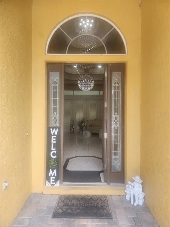 An open front door reveals a tiled entryway with a crystal chandelier and arched transom window — 2656 WYNDSOR OAKS WAY, WINTER HAVEN, FL