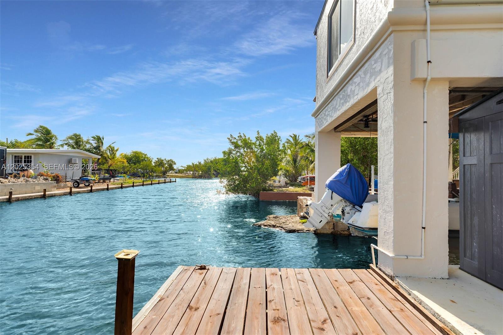 A wooden dock extends into a canal beside a house with a boat lift — BIG PINE, FL