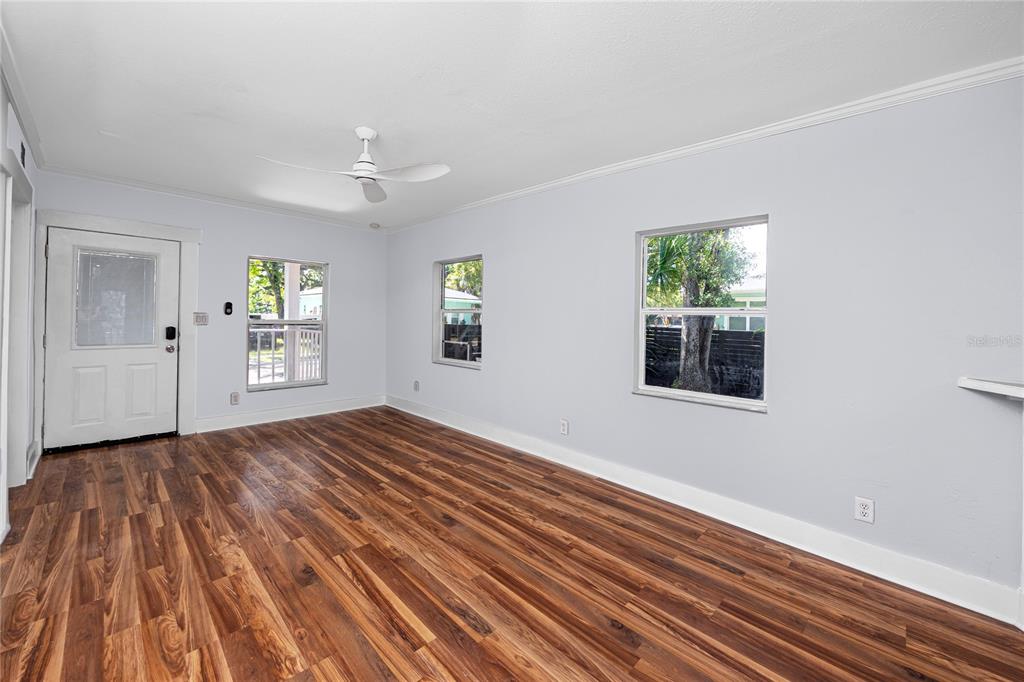 An empty room features light gray walls, wood-look flooring, a ceiling fan, and three windows — 1763 PRESTON STREET S, ST PETERSBURG, FL