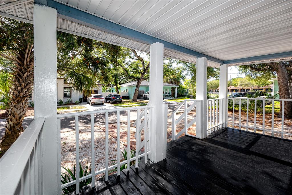 A covered wooden porch features white railings and posts overlooking a residential street — 1763 PRESTON STREET S, ST PETERSBURG, FL