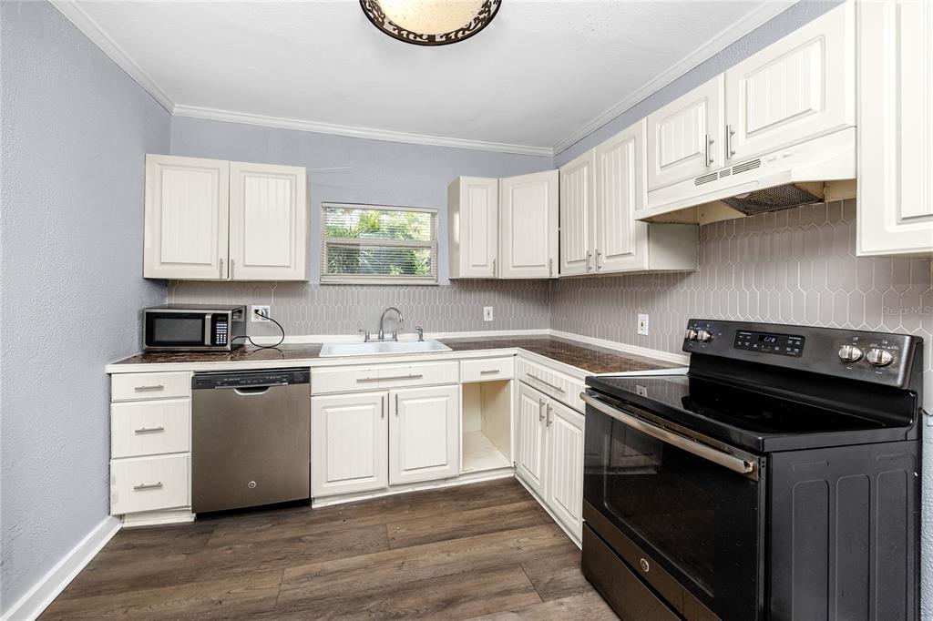 A kitchen features white cabinets, dark countertops, stainless steel appliances, and wood-look flooring — 1763 PRESTON STREET S, ST PETERSBURG, FL
