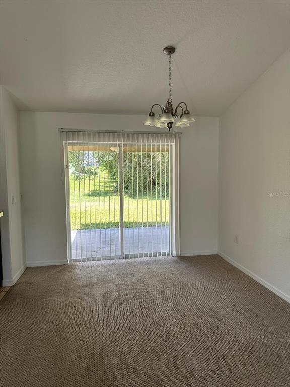 A dining area with beige carpet, white walls, a chandelier, and sliding glass patio doors — 2149 N NORMANDY BOULEVARD, DELTONA, FL