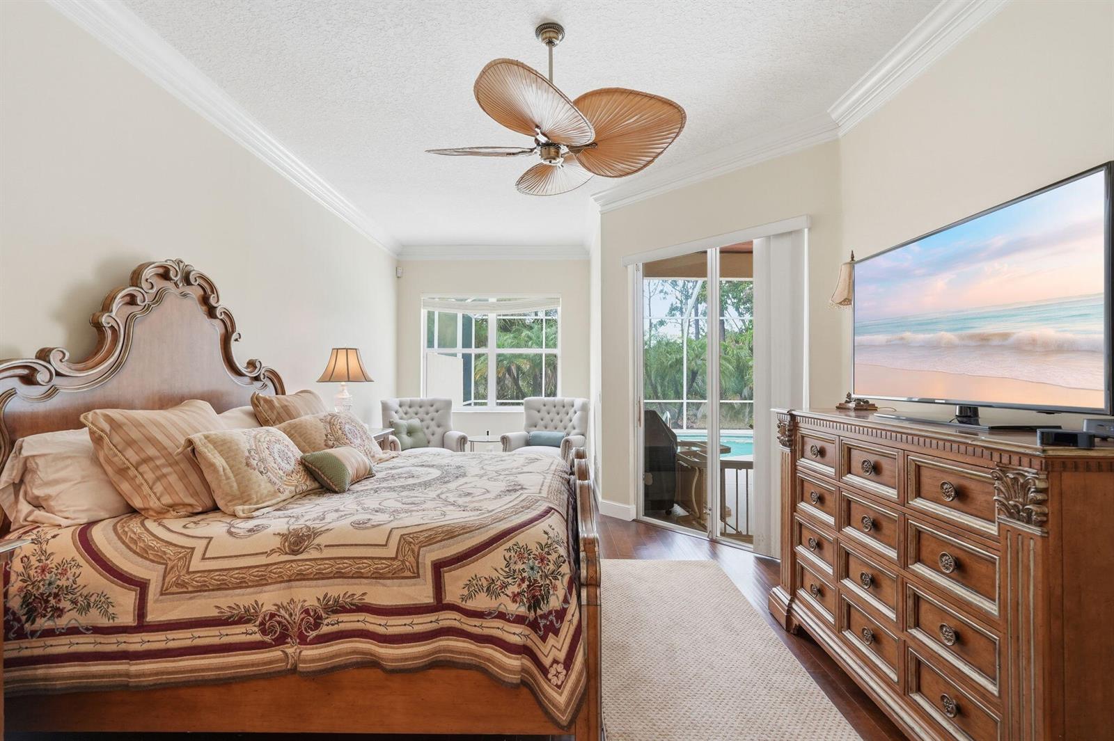 A bedroom features a large wooden bed, a dresser with a television, and sliding glass doors — 6483 SE Wild Olive Lane, Stuart FL 34997, STUART, FL