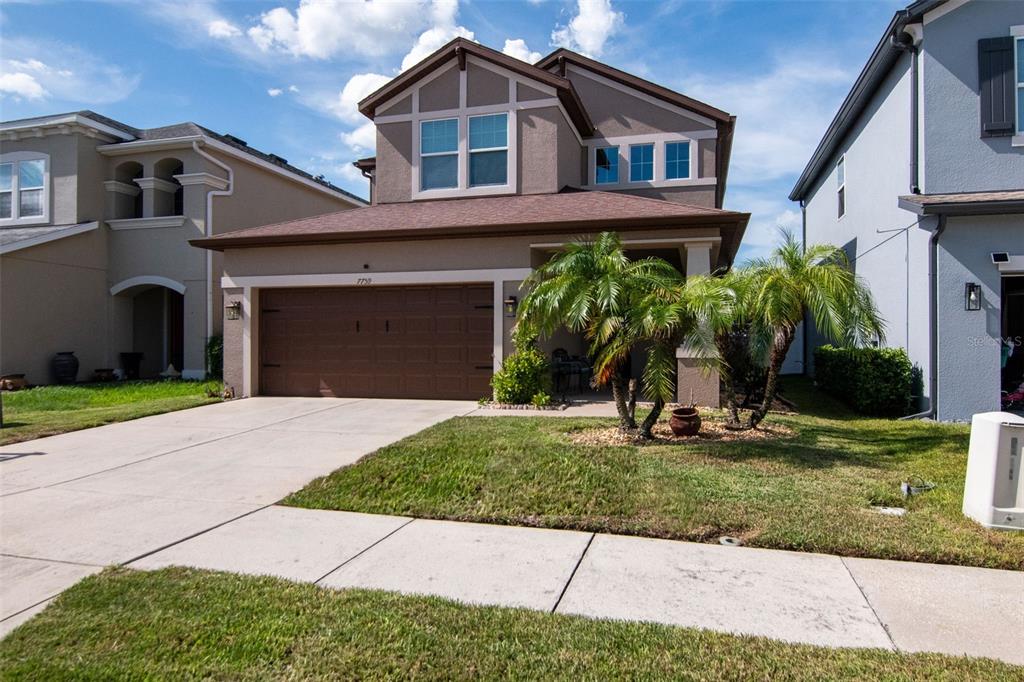 A two-story suburban house with a brown garage, tan stucco exterior, and palm trees — 7759 WINDCHASE WAY, WESLEY CHAPEL, FL