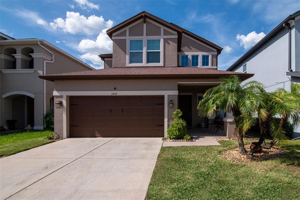 A two-story suburban house with a brown garage door, tan stucco exterior, and palm tree — 7759 WINDCHASE WAY, WESLEY CHAPEL, FL