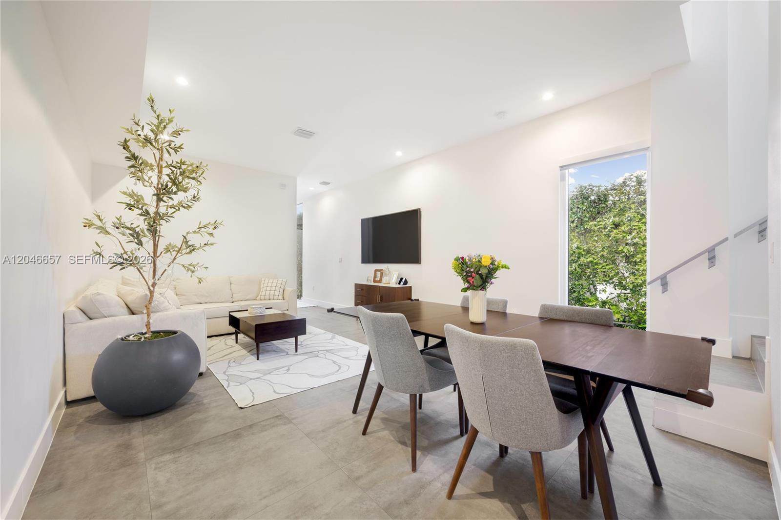 A modern open-concept living and dining area features tile floors, a white sofa, and stairs — 3655 SW 25th St # 3655, Miami FL 33133, MIAMI, FL