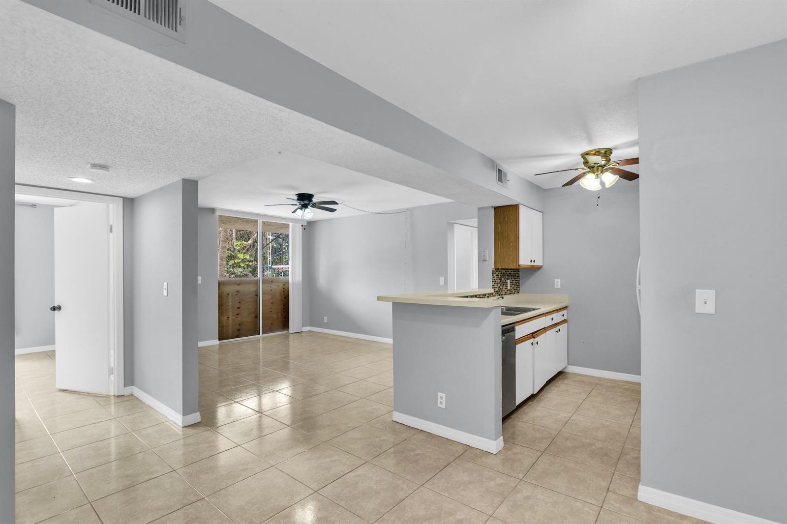 An open-concept kitchen and living area feature light gray walls, tile flooring, and ceiling fans — 3995 W Mcnab Road # B205, Pompano Beach FL 33069, POMPANO BEACH, FL