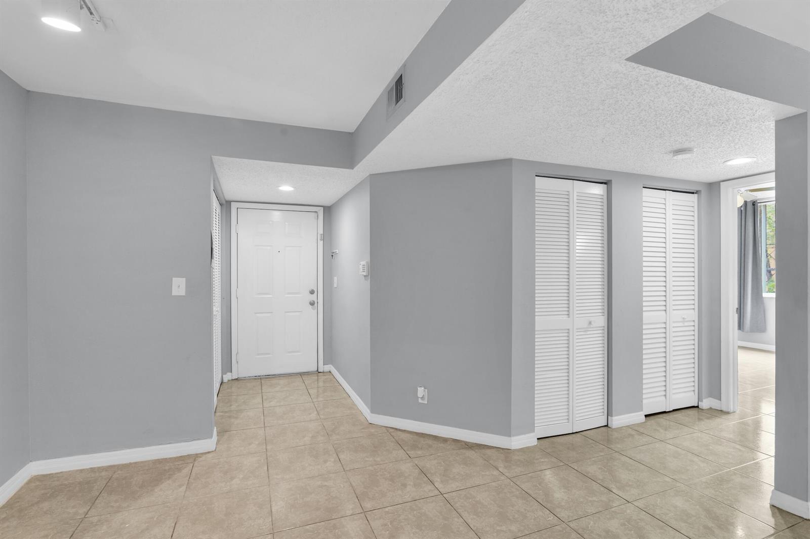 An entryway with light-colored tile flooring, gray walls, and white louvered closet doors — 3995 W Mcnab Road # B205, Pompano Beach FL 33069, POMPANO BEACH, FL