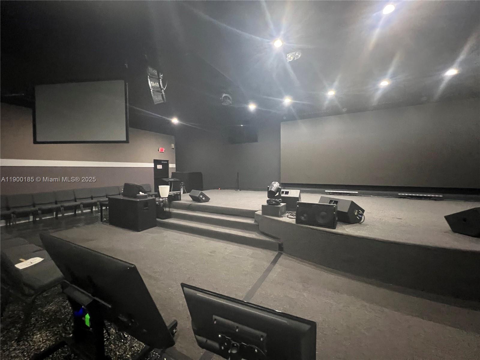A stage with audio equipment and screens sits in a dark, carpeted auditorium room — 3800 N University Dr # 3846, Sunrise FL 33351, SUNRISE, FL
