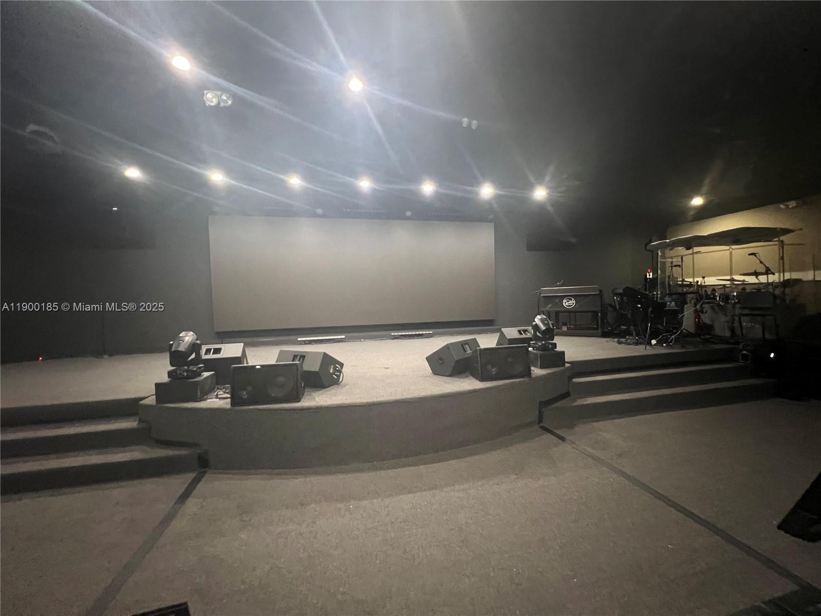 A stage with audio equipment and a large screen in a dark, carpeted room — 3800 N University Dr # 3846, Sunrise FL 33351, SUNRISE, FL