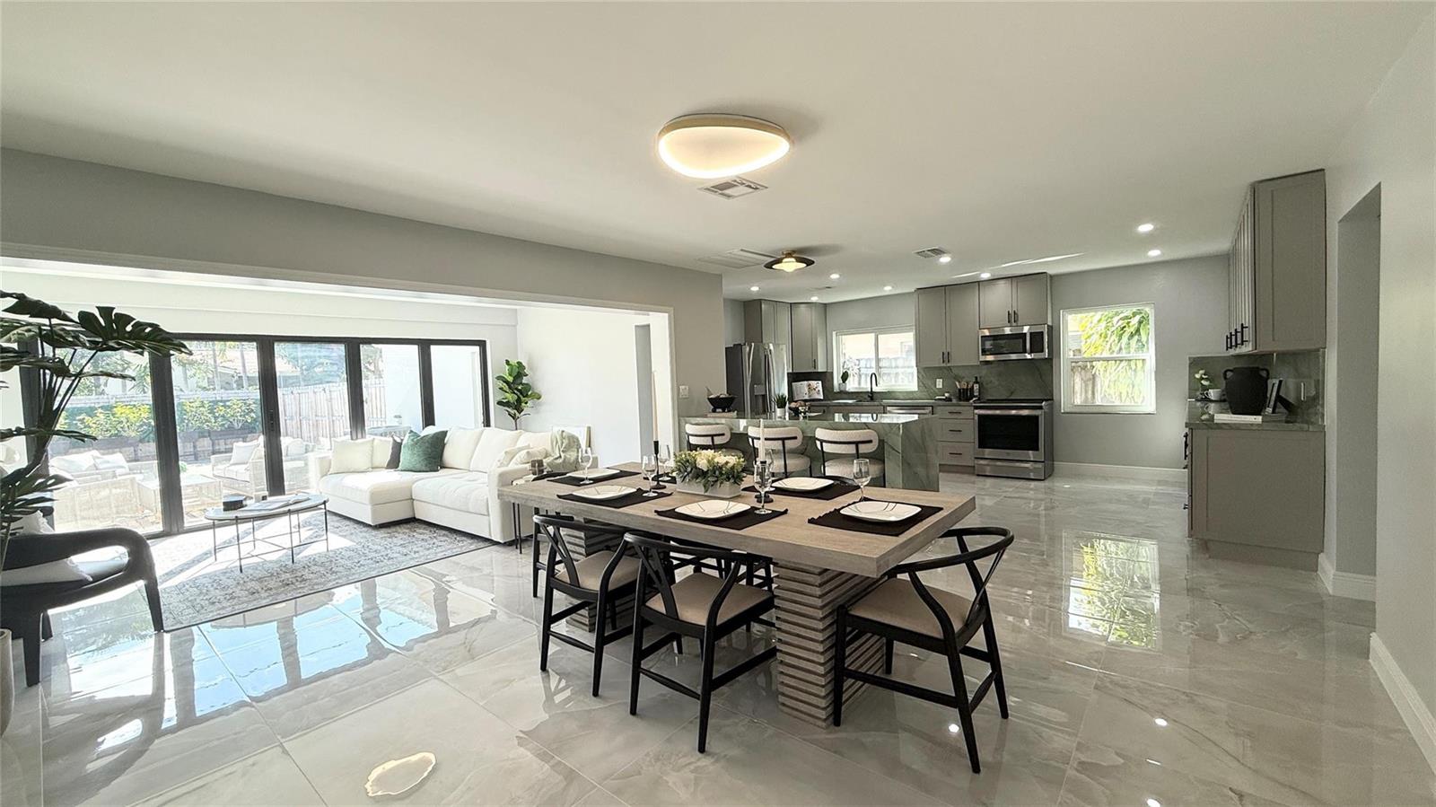 An open-concept living and dining area features gray cabinetry, marble-look tile floors, and sliding doors — 1424 Adams Street, Hollywood FL 33020, HOLLYWOOD, FL