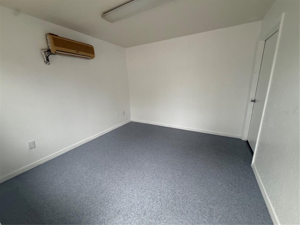 An empty room with white walls, gray carpet, a wall-mounted air conditioner, and a door — 4534 NE 35TH STREET UNIT 5, OCALA, FL