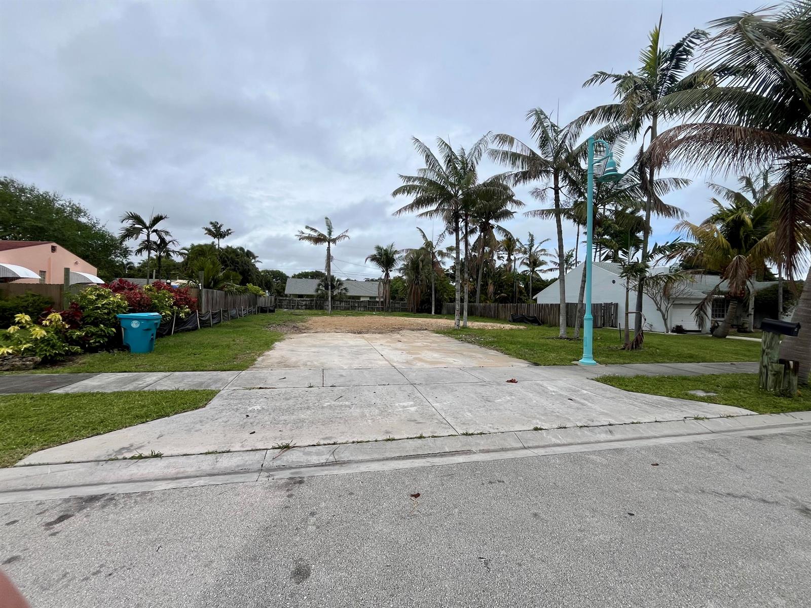 A vacant residential lot features a concrete driveway and several palm trees under a cloudy sky — 647 NE 9th Avenue, Boynton Beach FL 33435, BOYNTON BEACH, FL