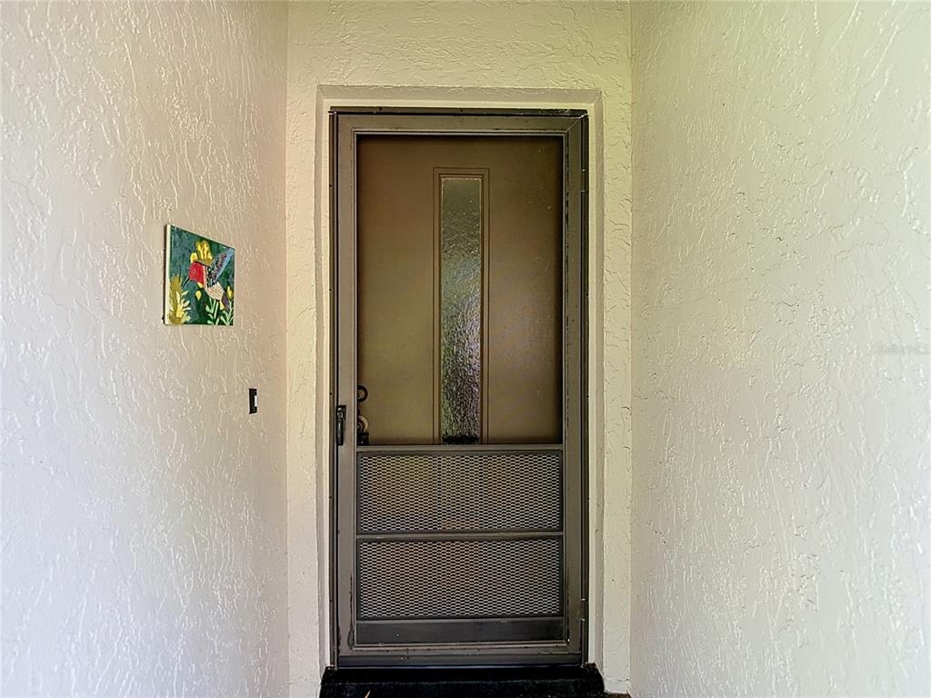 A brown storm door with a glass panel and metal screen sits in a recessed entryway — 13010 WEDGEWOOD WAY UNIT C, HUDSON, FL