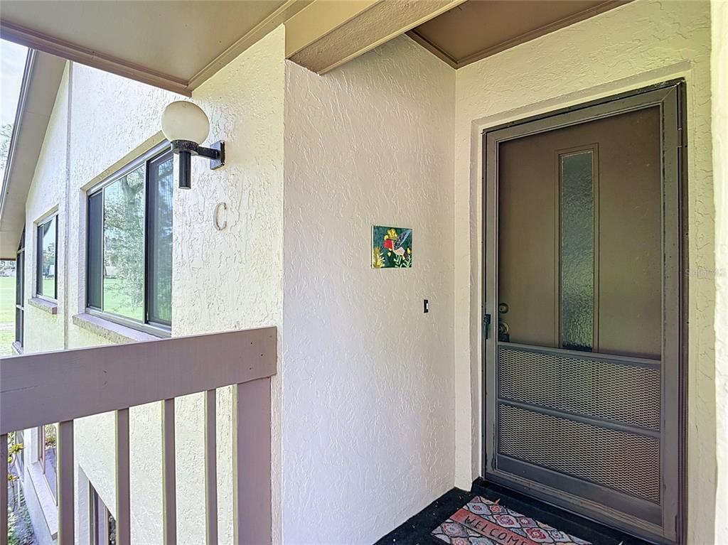 An exterior view of a building entrance featuring a brown storm door and a balcony railing — 13010 WEDGEWOOD WAY UNIT C, HUDSON, FL
