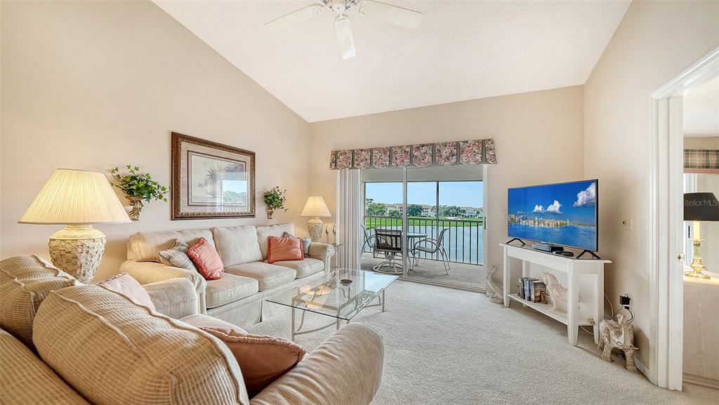 A living room with a beige sofa, glass coffee table, television, and a balcony view — 9330 CLUBSIDE CIRCLE UNIT 3306, SARASOTA, FL