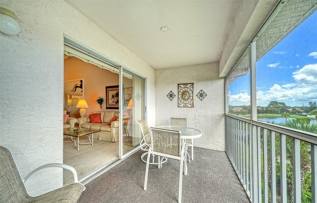 A screened-in balcony features a small dining set, wall decor, and views of a pond — 9330 CLUBSIDE CIRCLE UNIT 3306, SARASOTA, FL