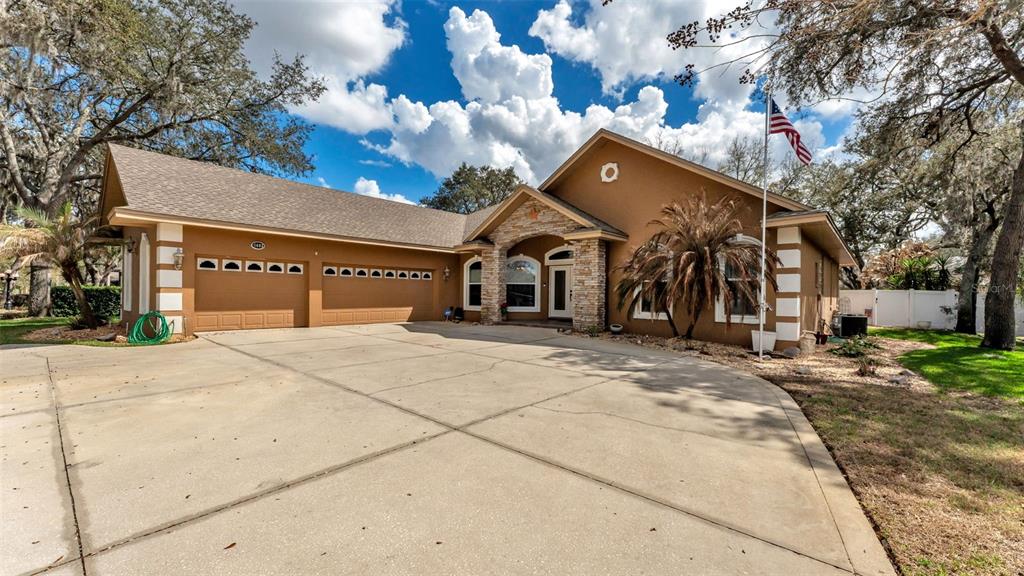 A tan single-story house with a stone-accented entryway, a three-car garage, and a large driveway — 1603 SIR HENRYS TRAIL, LAKELAND, FL