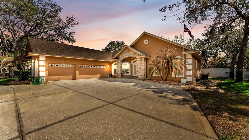 A single-story house with a tan stucco exterior, stone accents, and a large concrete driveway — 1603 SIR HENRYS TRAIL, LAKELAND, FL