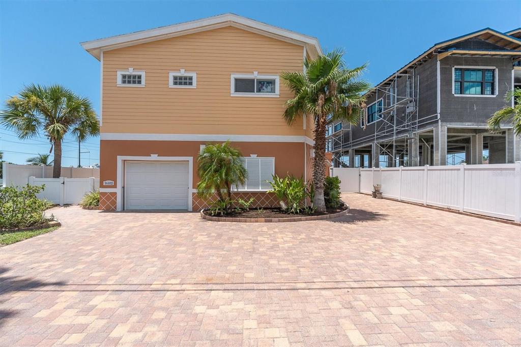 A two-story house with a garage and paved driveway sits next to a construction site — 16102 4TH STREET E, REDINGTON BEACH, FL