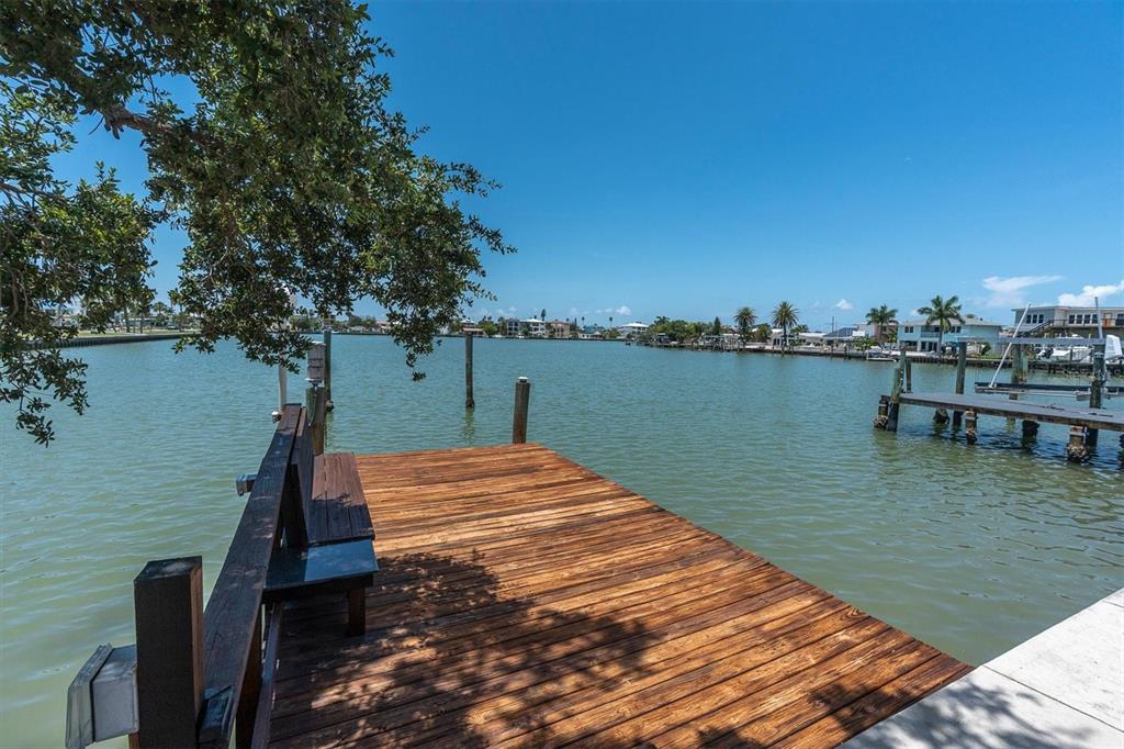 A wooden dock with a built-in bench overlooks a calm canal with distant waterfront homes — 16102 4TH STREET E, REDINGTON BEACH, FL