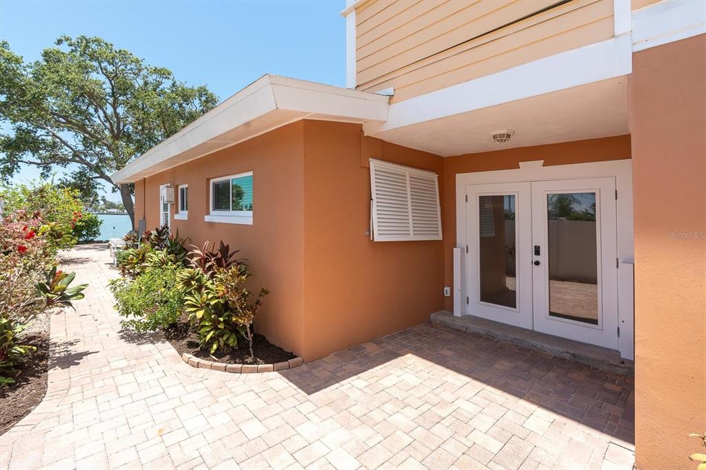 A paved patio leads to white French doors on the side of a tan house — 16102 4TH STREET E, REDINGTON BEACH, FL