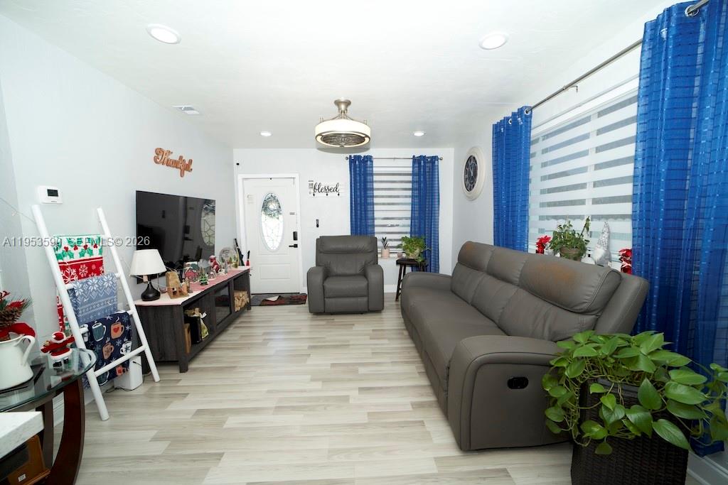 A living room features light wood-look flooring, a gray sofa, and bright blue curtains — 10910 SW 217th Ter, Miami FL 33170, MIAMI, FL