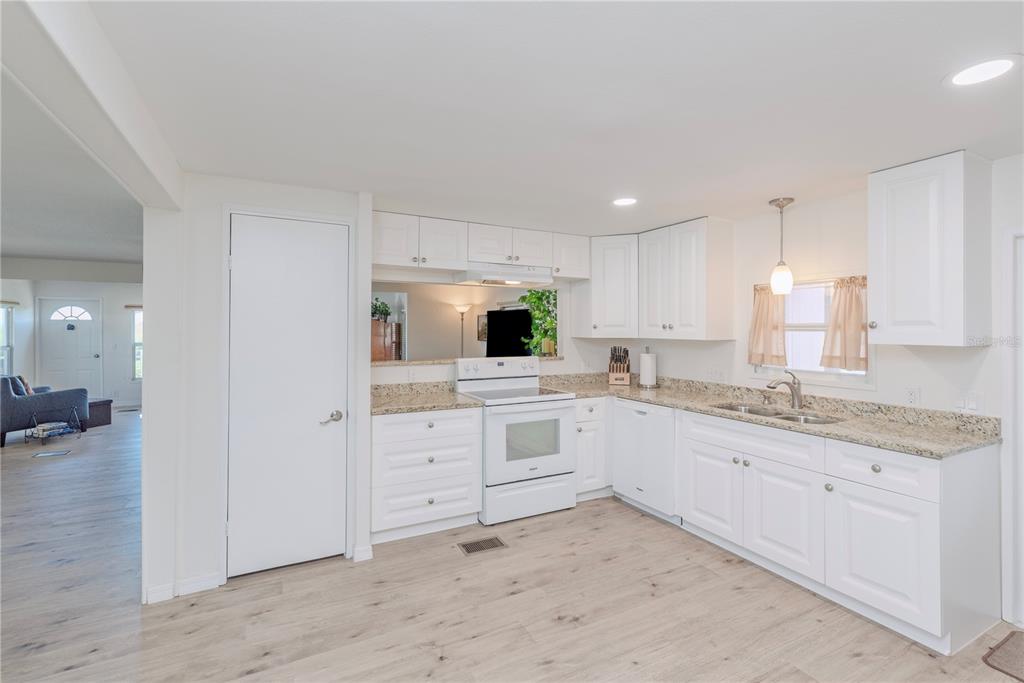 A kitchen features white cabinets, granite countertops, white appliances, and light wood-look flooring — 4851 W GANDY BOULEVARD UNIT 23C, TAMPA, FL