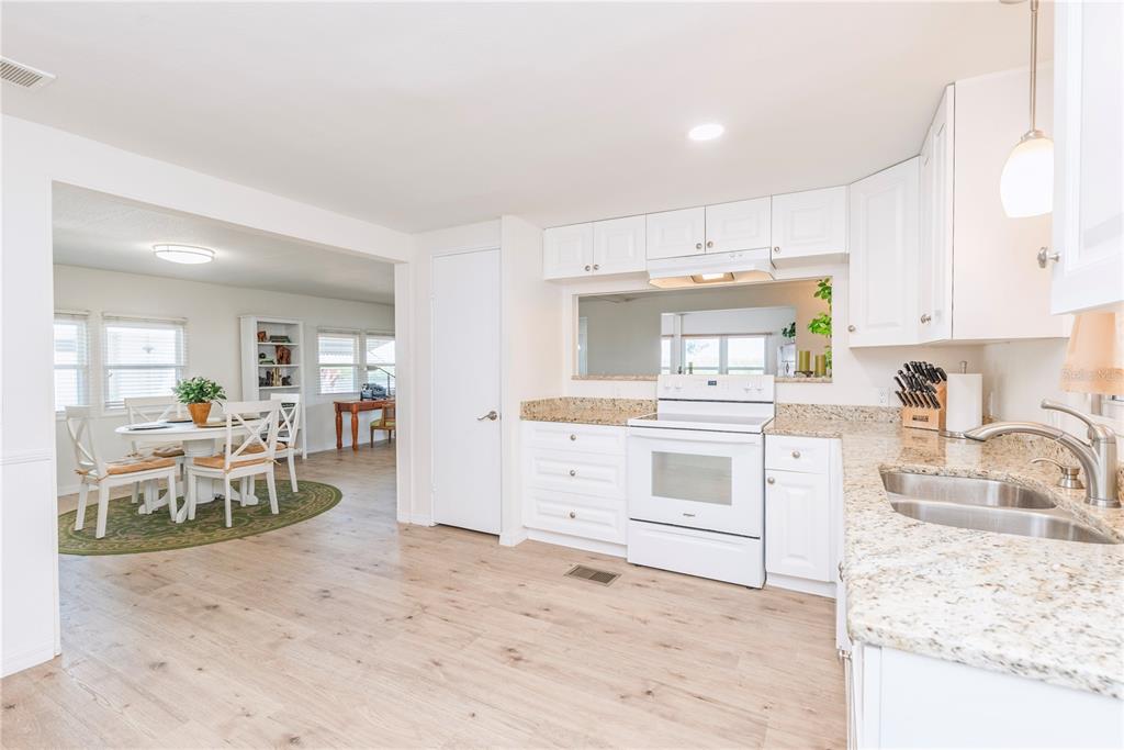 A kitchen with white cabinets and granite countertops opens into a dining area with wood flooring — 4851 W GANDY BOULEVARD UNIT 23C, TAMPA, FL