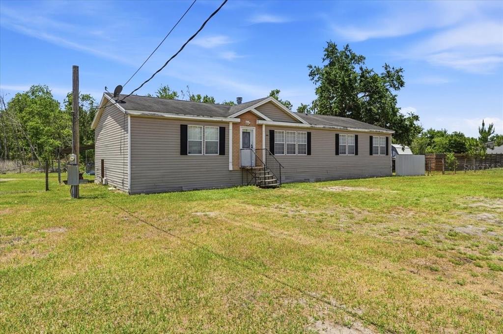 A single-story manufactured home with beige siding sits on a large, grassy lot — 10724 PATHFINDER TRAIL, LAKELAND, FL