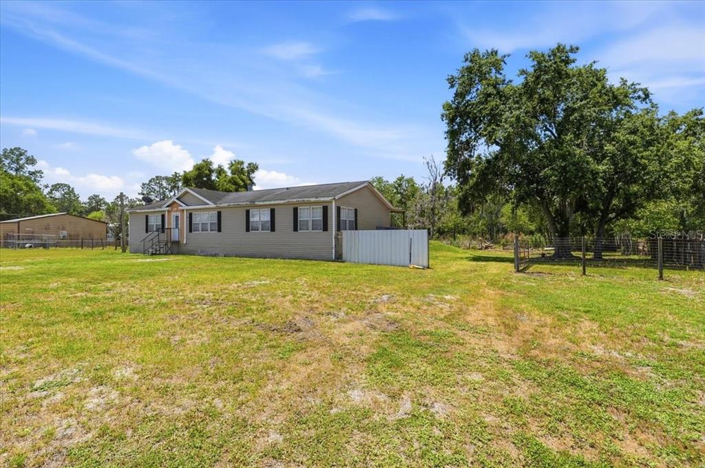 A single-story house with beige siding sits on a large, grassy lot with trees — 10724 PATHFINDER TRAIL, LAKELAND, FL