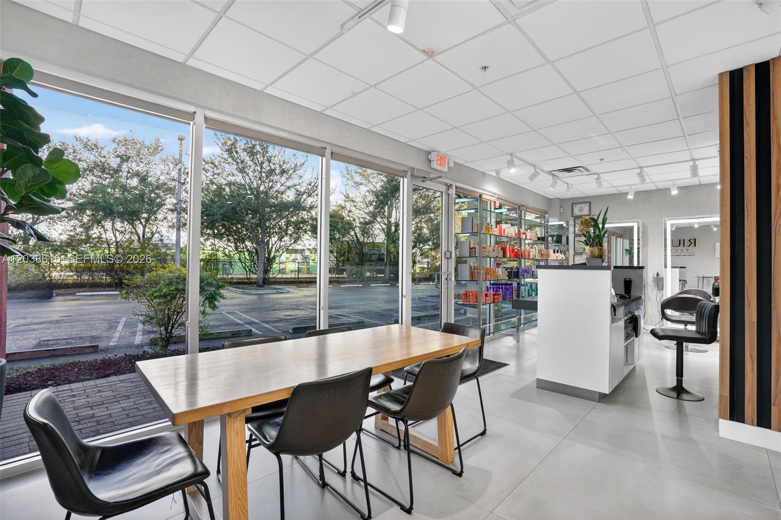 A modern salon interior features a wooden dining table, black chairs, and floor-to-ceiling windows — Second Generation Beauty Salon For Lease In Hialeah, FL 33015, FL
