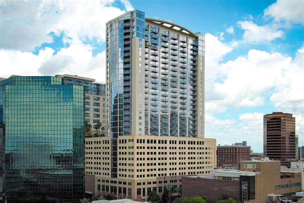 A tall, modern high-rise apartment building stands prominently among surrounding city office buildings — 155 S COURT AVENUE UNIT 1102, ORLANDO, FL