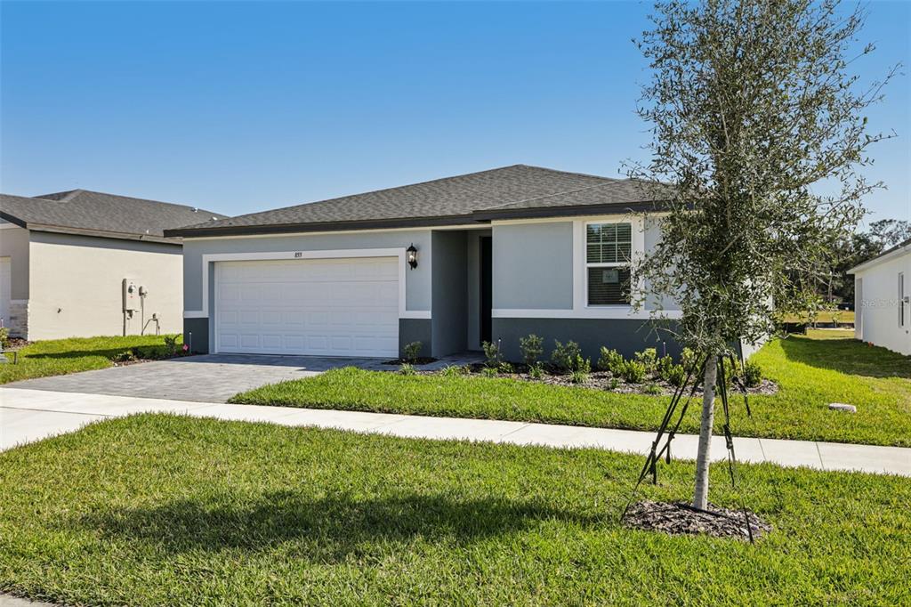 A single-story house with a two-car garage, gray exterior, and a paved driveway — 855 SUNSHOWER DRIVE, LADY LAKE, FL