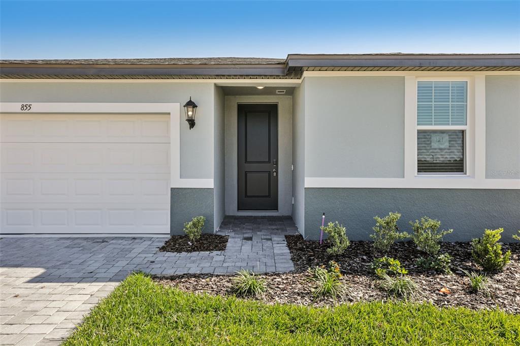 The exterior of a house features a white garage door, a dark front door, and landscaping — 855 SUNSHOWER DRIVE, LADY LAKE, FL