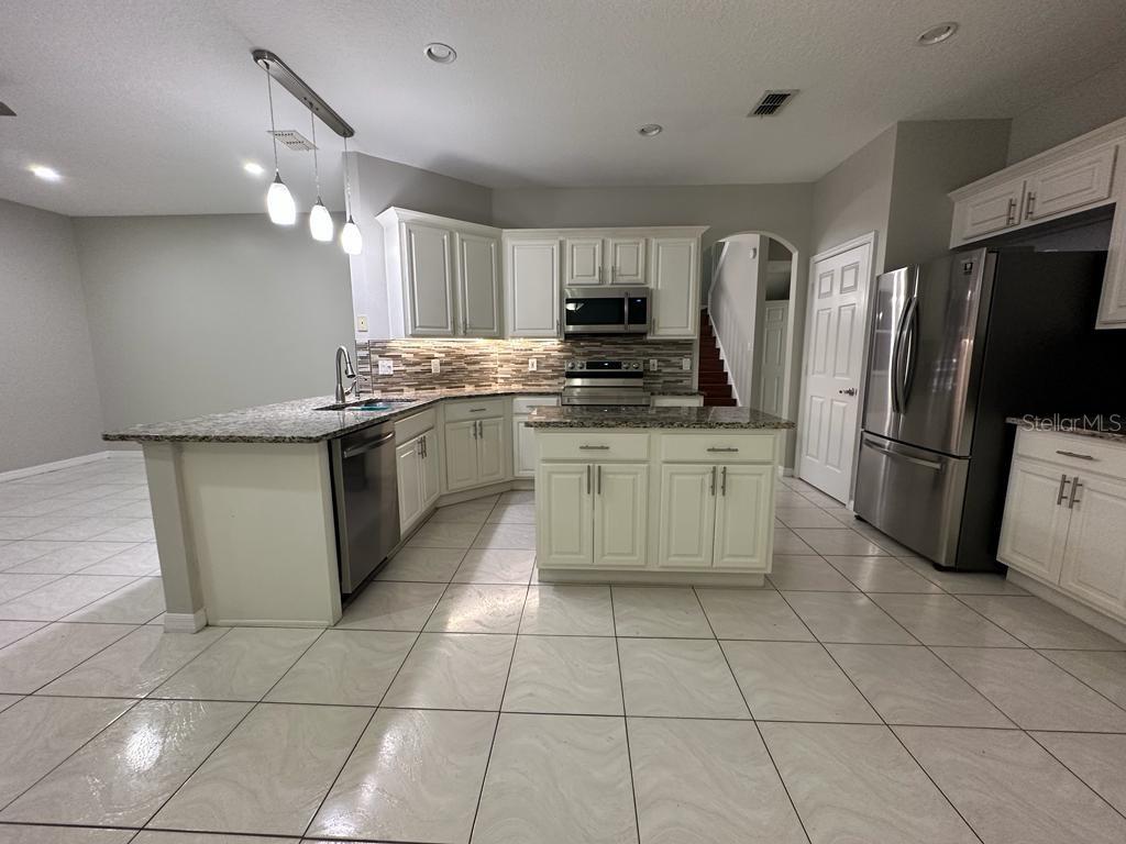 A kitchen features white cabinetry, granite countertops, stainless steel appliances, and light-colored tile flooring — 4743 CHALFONT DRIVE, ORLANDO, FL