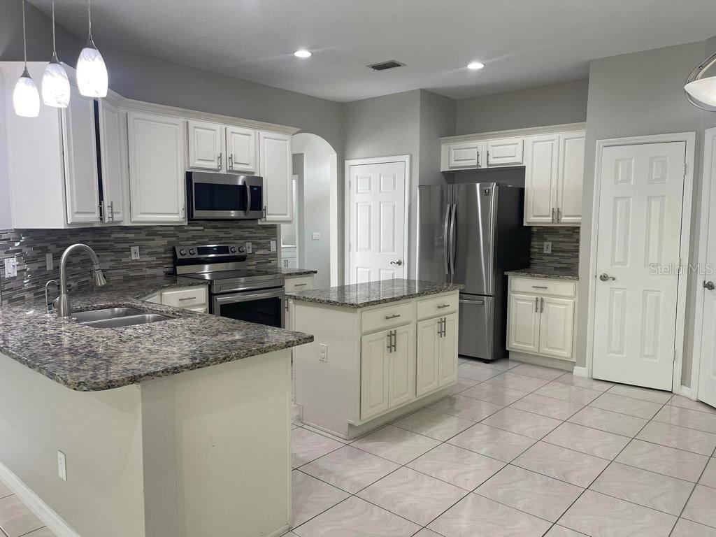 A kitchen features white cabinets, granite countertops, stainless steel appliances, and light-colored tile flooring — 4743 CHALFONT DRIVE, ORLANDO, FL