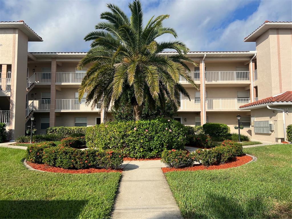 A three-story apartment building features a central palm tree and a landscaped garden path — 6501 STONE RIVER ROAD UNIT 309, BRADENTON, FL