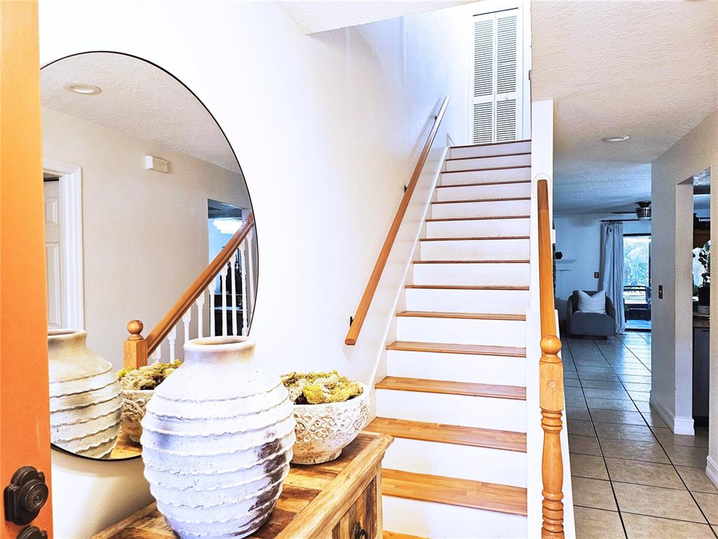 A foyer features a wooden staircase, a round mirror, and a textured vase on a console — 446 CLUB DRIVE, WINTER SPRINGS, FL