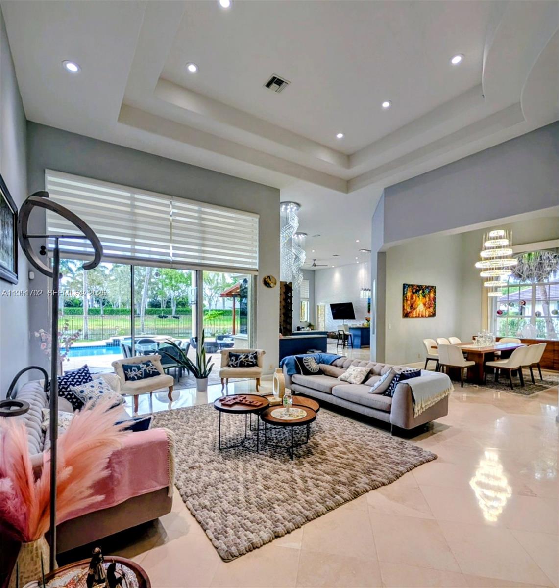 A spacious living room with high tray ceilings, tile floors, and a view of a pool — 104 Dockside Cir, Weston FL 33327, WESTON, FL
