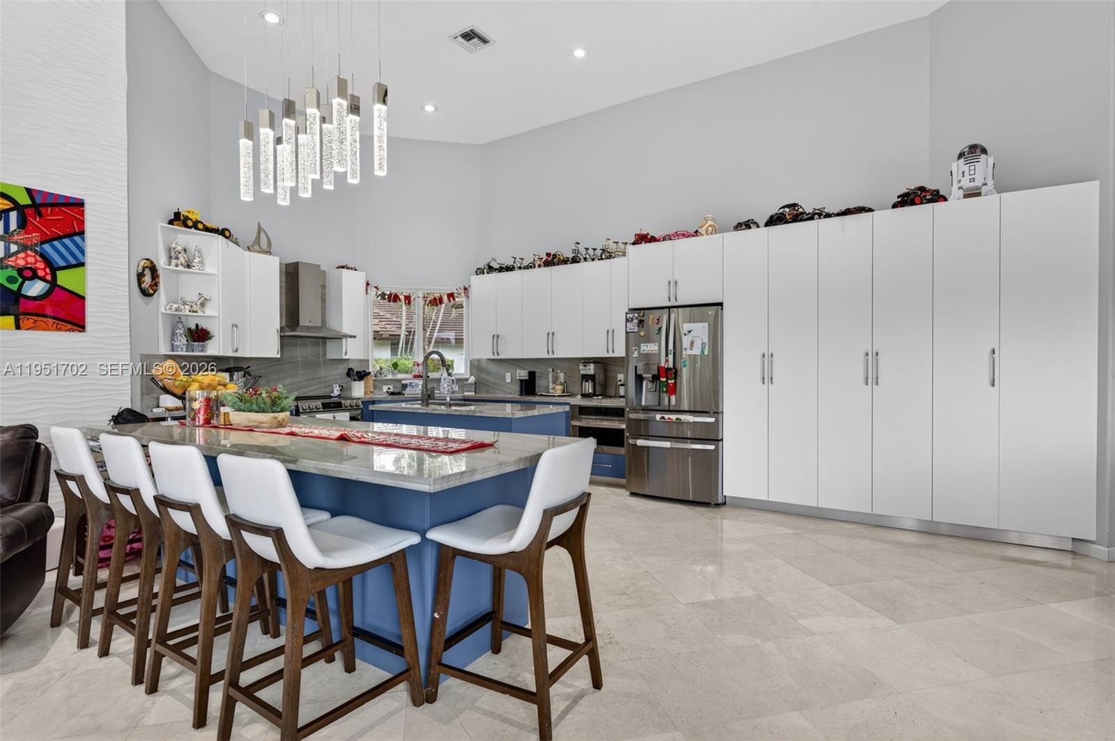 A modern kitchen features a blue island, white cabinetry, and a high vaulted ceiling — 104 Dockside Cir, Weston FL 33327, WESTON, FL