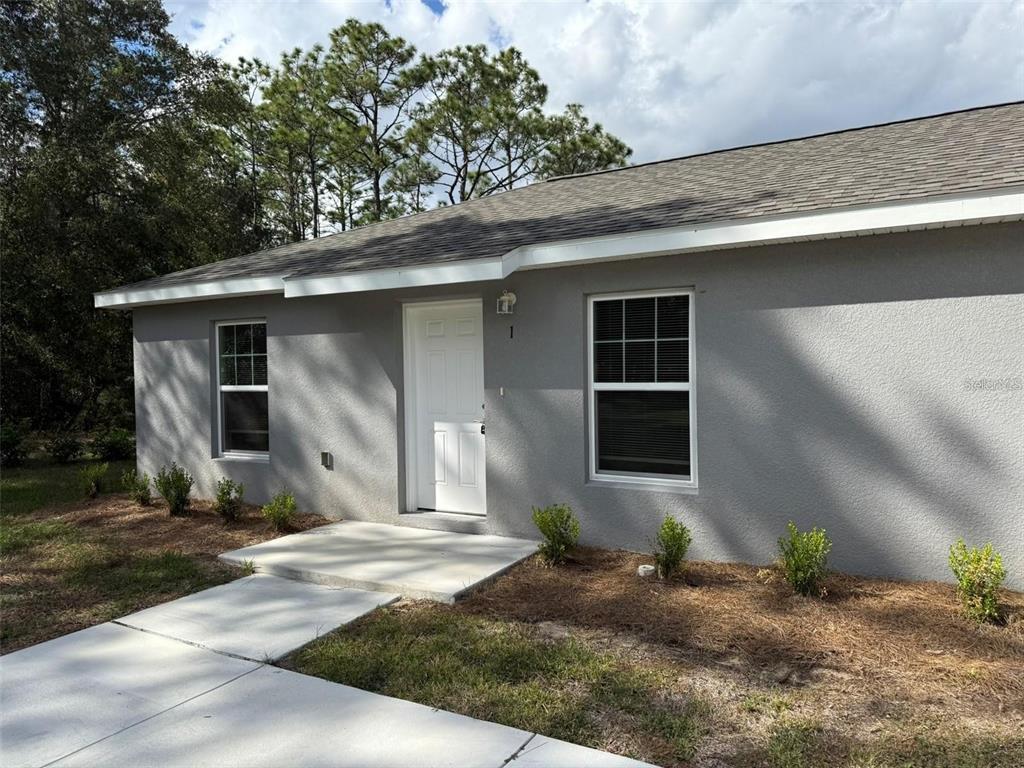 A gray stucco house exterior features a white front door, two windows, and a walkway — 9541 N TRAVIS DRIVE UNIT A, CITRUS SPRINGS, FL