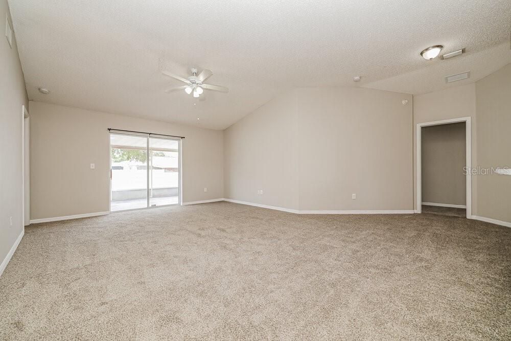 An empty living room features beige carpet, vaulted ceilings, a ceiling fan, and sliding glass doors — 11025 WHITTNEY CHASE DRIVE, RIVERVIEW, FL